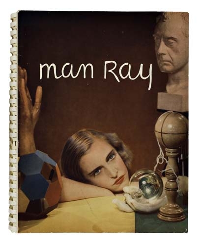 A surreal still life featuring a reclining figure, a sculpted head, and geometric objects against a dark background.