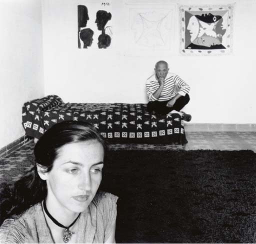 A black-and-white interior scene featuring a close-up of a woman in the foreground and a man sitting on a bed in the background.