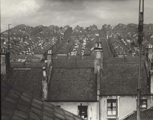 A black-and-white photograph capturing a dense urban neighborhood with rows of terraced houses stretching into the distance.