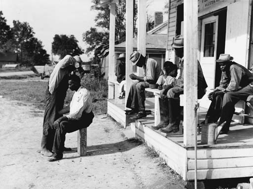 Negroes cut each others hair in front of plantation store after being paid off on Saturday, Milestone Plantation, Mississippi Delta by Marion Post Wolcott, 1939
