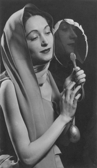 A black-and-white portrait of a figure in a draped head covering holding a small mirror, capturing a moment of quiet reflection.