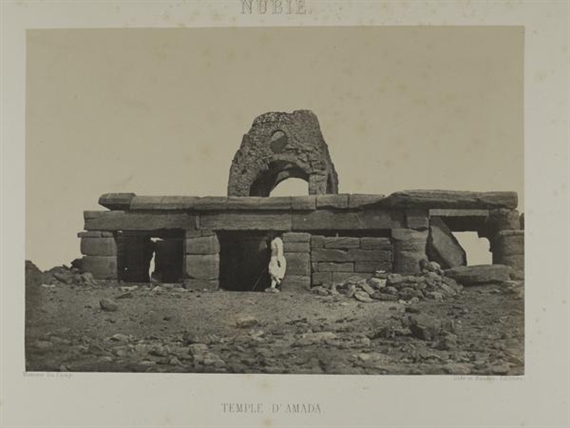 A sepia-toned photograph of ancient stone ruins with a figure standing in the doorway.