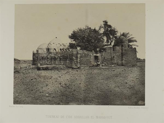 A sepia-toned photograph of a weathered stone structure with domes and trees, set against an open landscape.