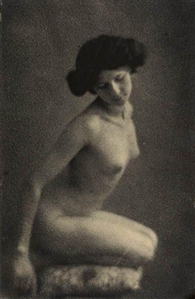 A monochromatic portrait of a seated figure with dark hair, captured in soft focus against a textured background.