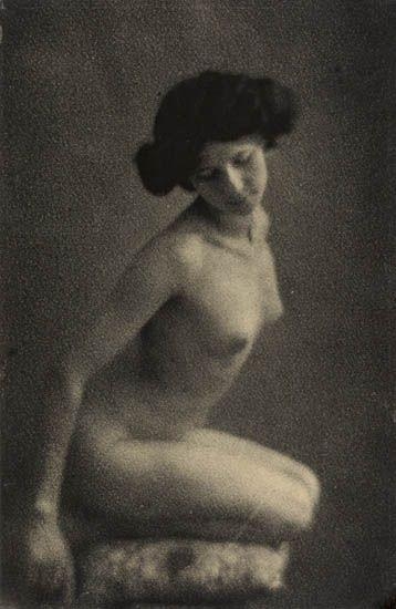 A monochromatic portrait of a seated figure with dark hair, captured in soft focus against a textured background.