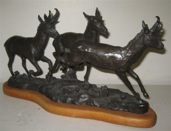 A bronze sculpture of three deer in motion on a wooden base.
