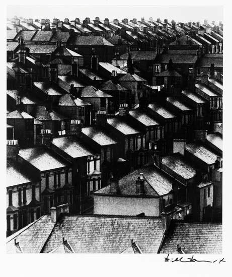 A black-and-white photograph of a dense urban neighborhood viewed from above.