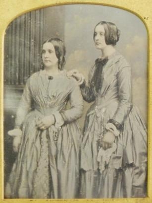 A hand-coloured half-plate daguerrotype depicting two ladies in elegant dress standing three quarter-length by William Edward Kilburn