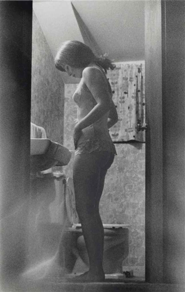 A candid black-and-white photograph capturing a figure standing in a bathroom.