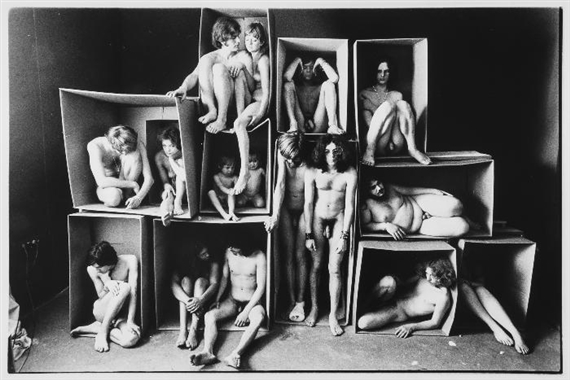 A black and white photograph of multiple figures posed inside and around a stack of cardboard boxes.
