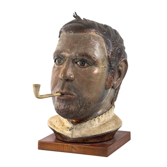 A sculpted bust of a man with a pipe, rendered in textured bronze and mounted on wood.
