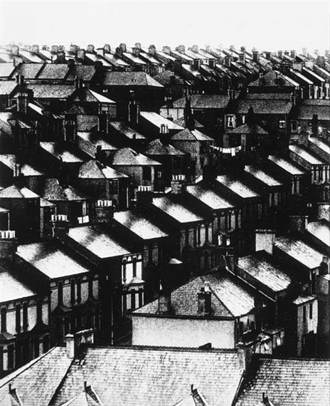 A black-and-white aerial view of a dense urban neighborhood filled with tightly packed houses and chimneys.