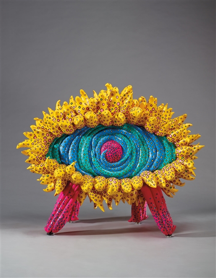 A vibrant, eye-shaped sculpture with a sunflower-like rim and pink legs.