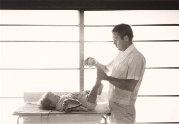 Steve McQueen at home putting slippers on daughter Terry by Sid Avery, 1960