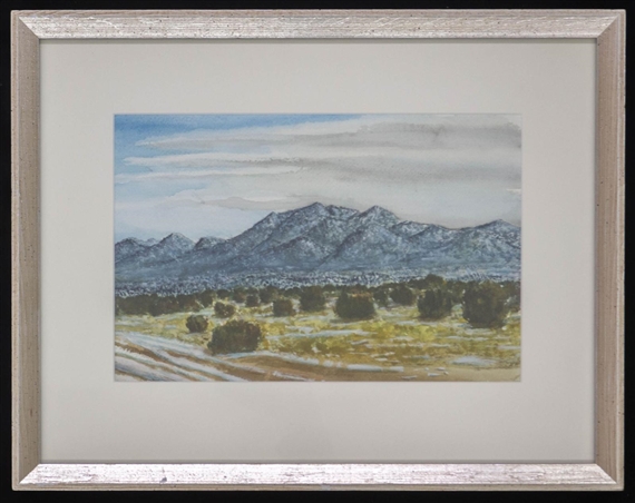 A framed landscape painting of a desert valley with snow-capped mountains under a cloudy sky.