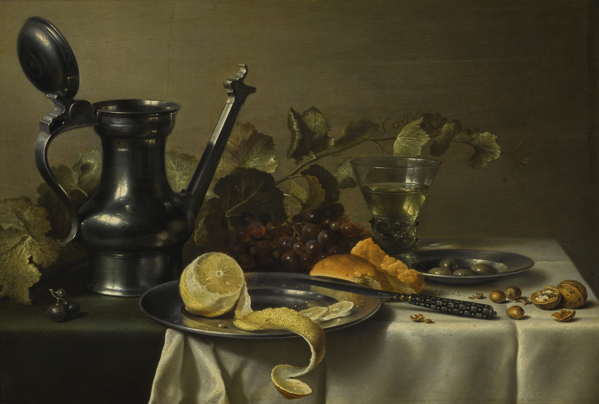 STILL LIFE WITH A 'JAN STEEN' JUG, A PEELED LEMON ON A PEWTER PLATE, BREAD, A KNIFE, OLIVES ON A PEWTER PLATE, GRAPES, A GLASS AND NUTS, ALL ON A TABLE PARTLY DRAPED WITH A WHITE CLOTH by Pieter Claesz
