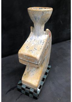 A ceramic sculpture resembling a stylized fish with a bowl on its back, featuring a speckled yellow glaze and a checkered base.