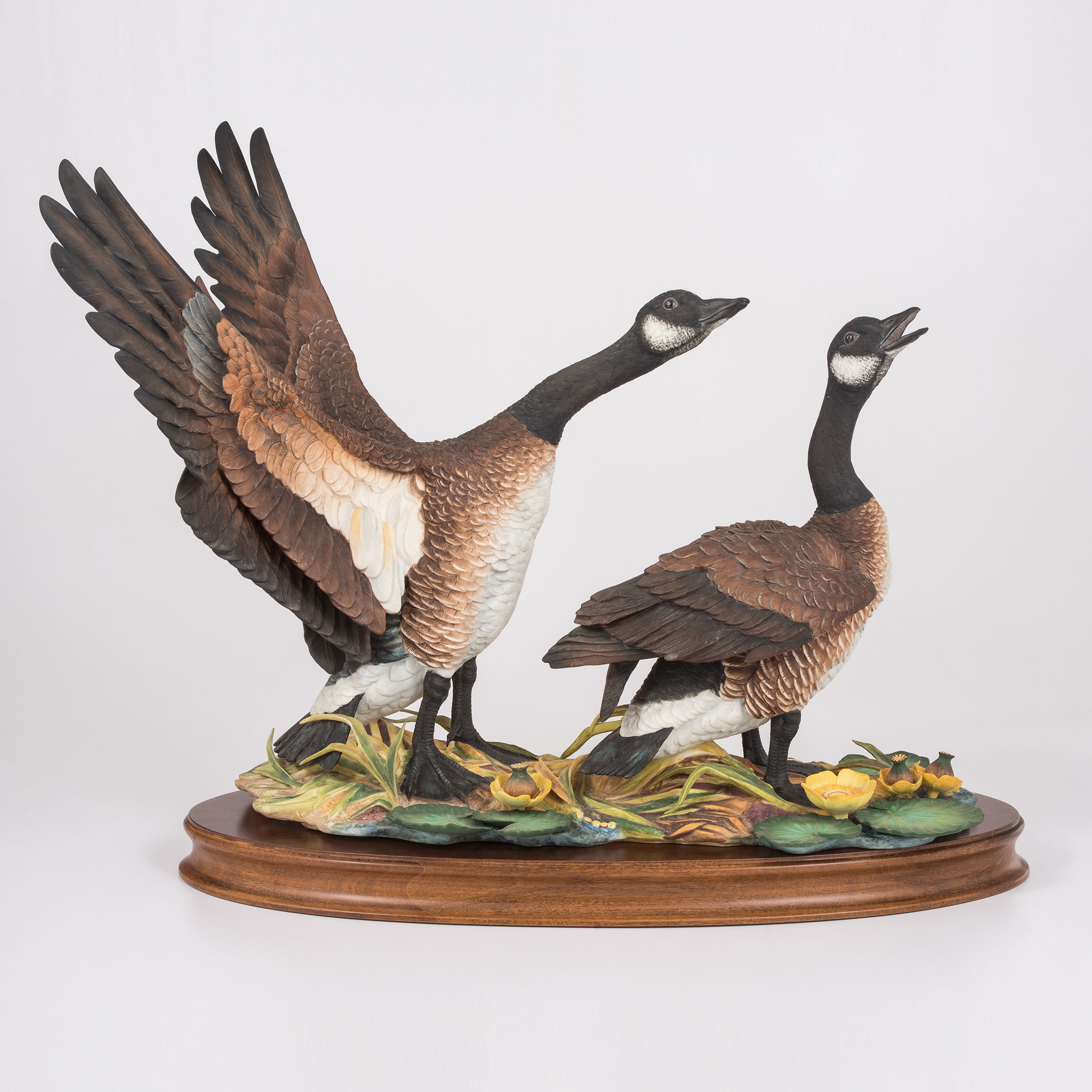 A sculptural pair of geese in dynamic poses on a naturalistic base.