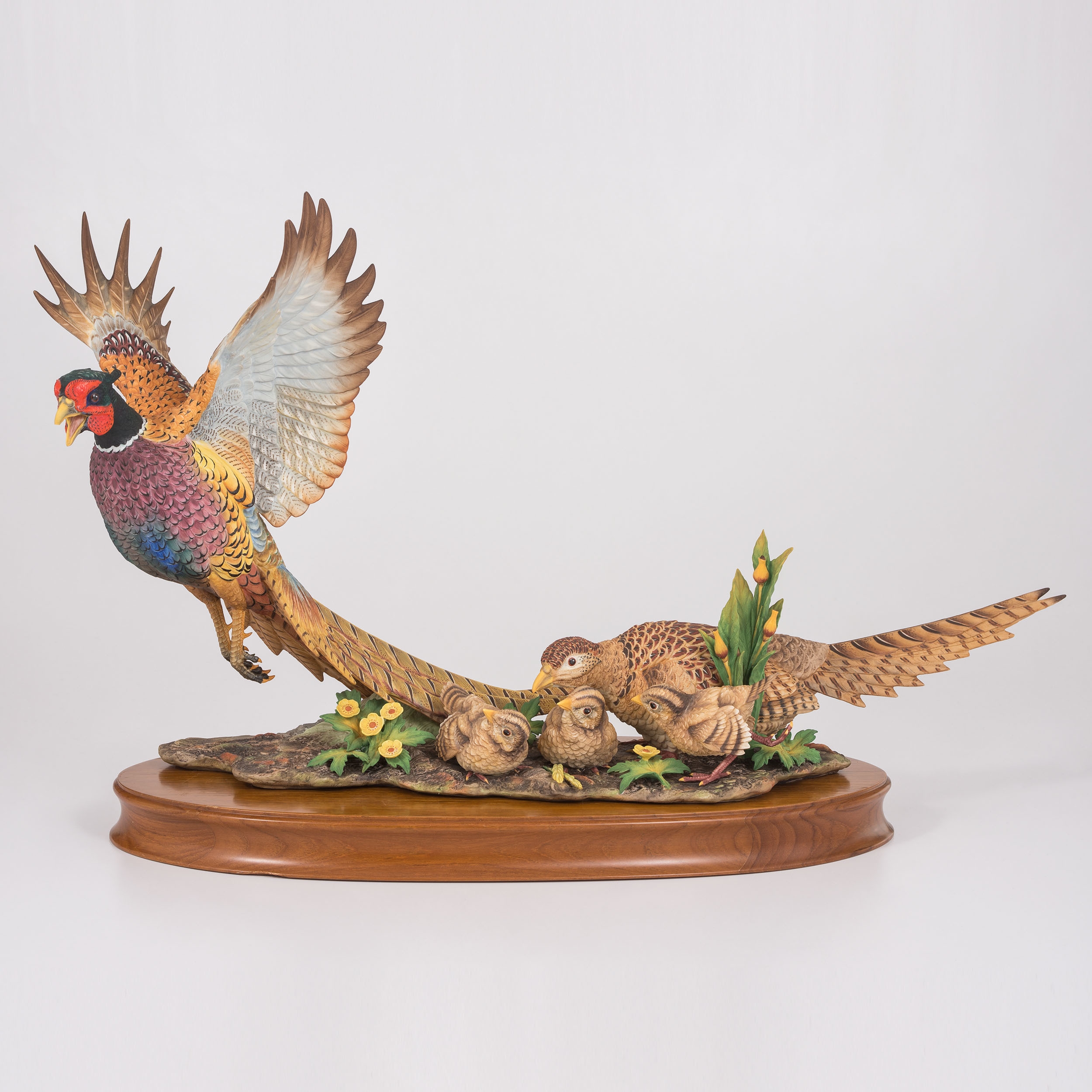 A sculptural group of pheasants in flight and rest, rendered in vibrant colors on a wooden base.
