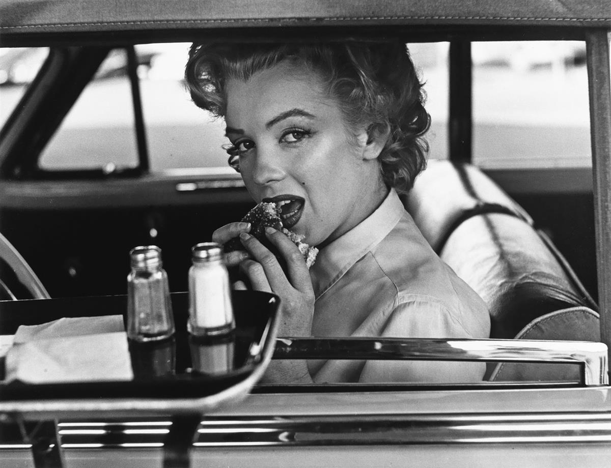 Marilyn Monroe eating a hamburger at a drive-in.