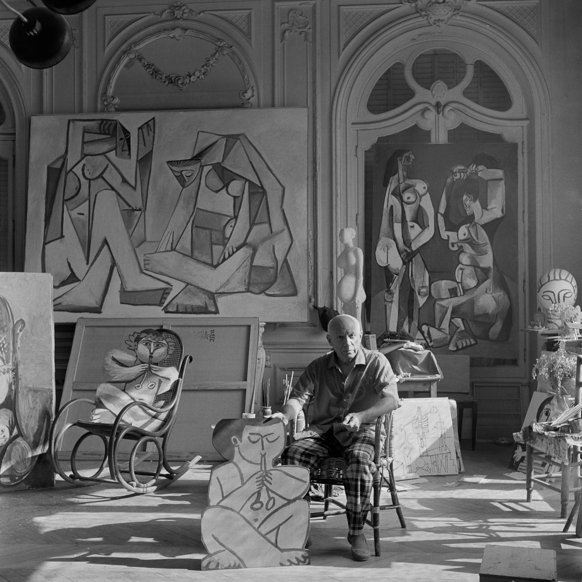 PABLO PICASSO HOLDING A CUTOUT FIGURE OF A FAUN, WITH ANOTHER FAUN 'SEATED' ON THE ROCKING CHAIR. BEHIND PABLO PICASSO, TWO PAINTINGS DONE IN . LA CALIFORNIE, CANNES by Edward Quinn, 1956