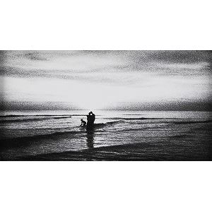 A black-and-white beach scene captures a person standing in the surf at twilight.
