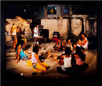 A candid night scene of a group of people gathered around a barbecue in an urban alleyway.