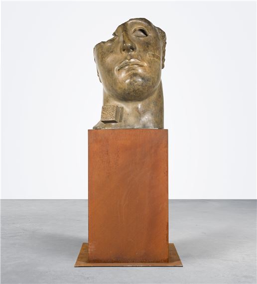 A bronze bust of a head resting on a rusted rectangular pedestal.