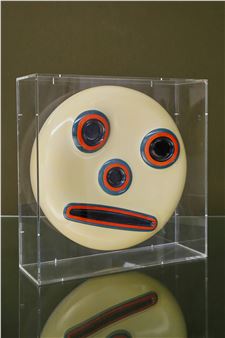 A minimalist sculpture of a stylized face with bold geometric features, enclosed in a transparent box.