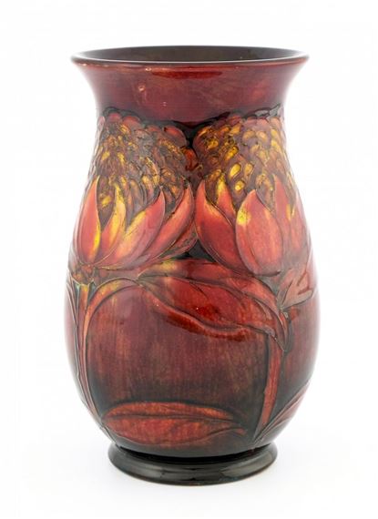 A glossy ceramic vase featuring a rich, earthy glaze with embossed floral motifs in warm reds and golds.