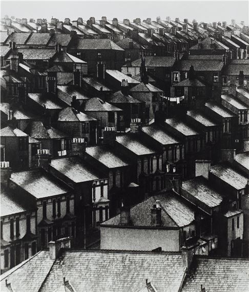 A high-angle black and white view of a dense urban neighborhood filled with uniform brick houses.