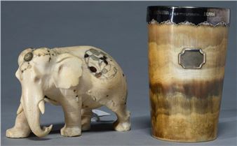 A detailed ivory elephant figurine stands beside a cylindrical horn vessel with silver inlay.