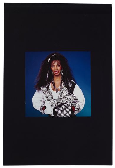 A portrait of a smiling woman with long dark hair, wearing a patterned vest over a white shirt, set against a solid blue background.
