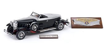 A black vintage convertible model car with a silver roof and chrome details sits next to a wooden plaque.
