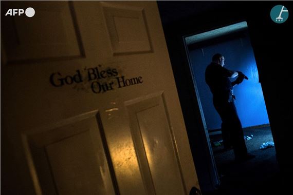 A police officer searching an abandoned house littered with syringes by Brendan Smialowski