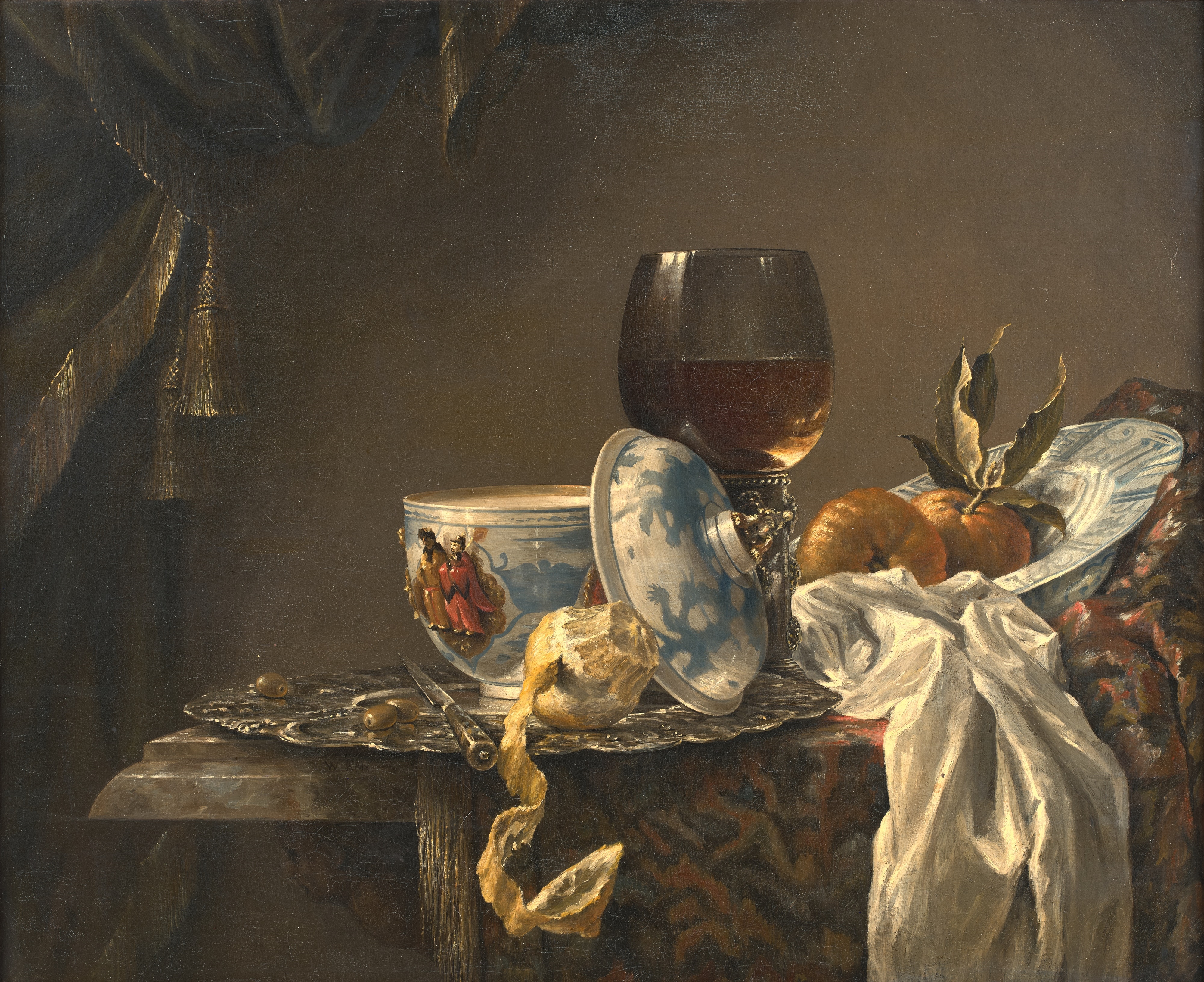 A still life of a silver platter with olives, a peeled lemon, an oriental bowl and cover, a roemer, and a bowl of fruit on a table draped with a tapestry by Willem Kalf