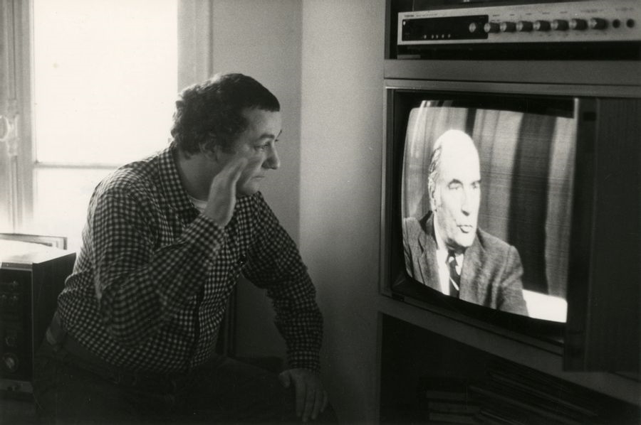 Coluche in front of his television set at a François Mitterrand press conference. Paris, December 8, 1980. - Léonard de Raemy