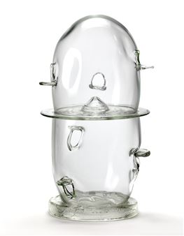 A transparent glass sculpture featuring a face-like form with metal handles.