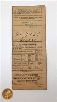 A vintage motor insurance receipt card with a gold coin in the foreground.