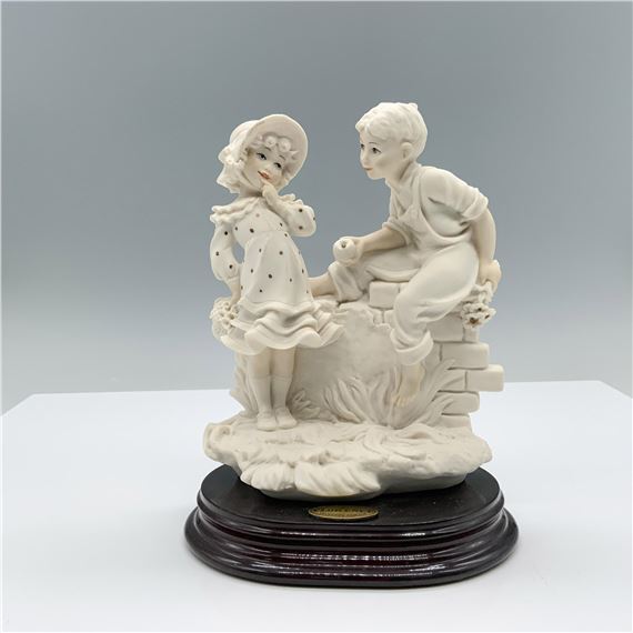 Fine crafted resin with white matte finish captures a young boy giving an apple to a young girl on top of a detailed wall