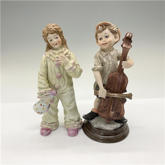 This pair includes a Milano porcelain sculpture by Eda of a girl dressed as a clown and a Giuseppe Armani style figurine of a boy playing a base. Both items are porcelain. Both pieces are similar in size