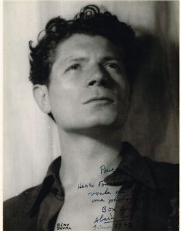 A black-and-white portrait of a person with dark curly hair gazing upward, wearing an open-collared shirt and bearing handwritten text across the chest.