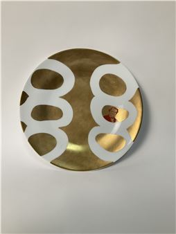 A minimalist circular artwork featuring bold white shapes on a metallic gold surface with a tiny red detail.