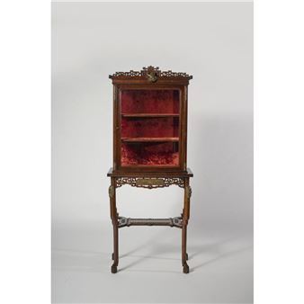 Vitrine en acajou mouluré et sculpté agrémentée d’éléments en bronze doré. La partie supérieure vitrée à deux étagères présente un fond garni de velours bordeaux. Elle ouvre à un vantail et repose sur une console à la ceinture ornée de motifs chinoisants à clairevoie, pieds galbés réunis par une tablette d’entretoise, se terminant en enroulements et présentant un décor de masques de lions bouddhiques en façade. La vitrine est surmontée d’une corniche à niche centrale d’où s’échappe une tête de d - Gabriel Viardot