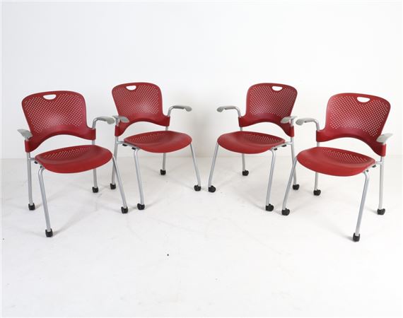 A studio shot of four identical red perforated chairs with silver metal frames arranged in a staggered row against a plain white background.