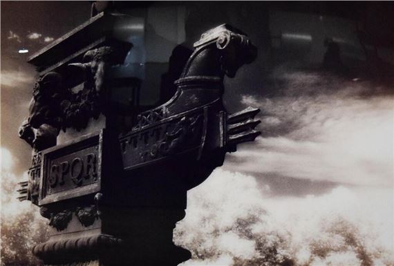 A dark, ornate sculpture with a horse head and lion motif stands against a cloudy sky.