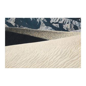 A close-up view of rippled sand dunes with distant mountains in the background.