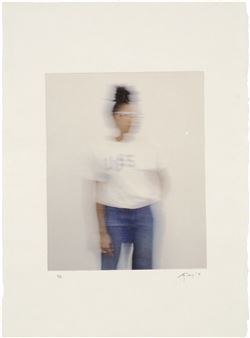 A motion-blurred portrait of a person in casual clothing against a plain background.