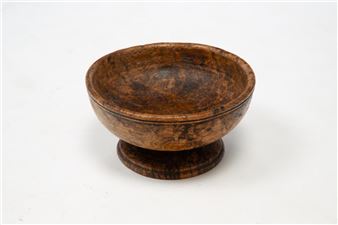 A rustic wooden bowl with a raised base, showcasing rich grain patterns and warm earth tones.