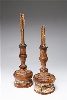 A pair of weathered wooden candlesticks with broken wax candles standing against a neutral background.